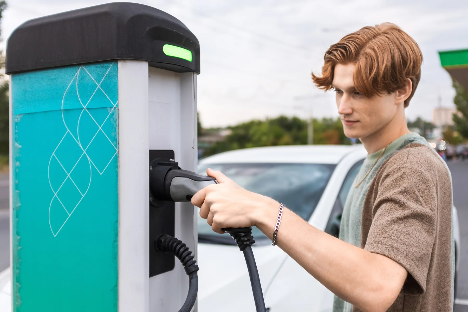A young man at a car charging station taking charger, electric car nearby in Chisinau, Moldova