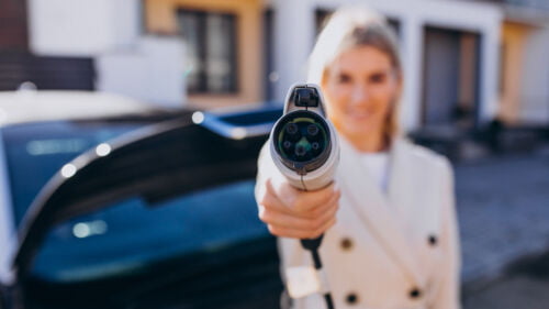 Wszystkie wiadomości - woman charging electro car by her house holding charger