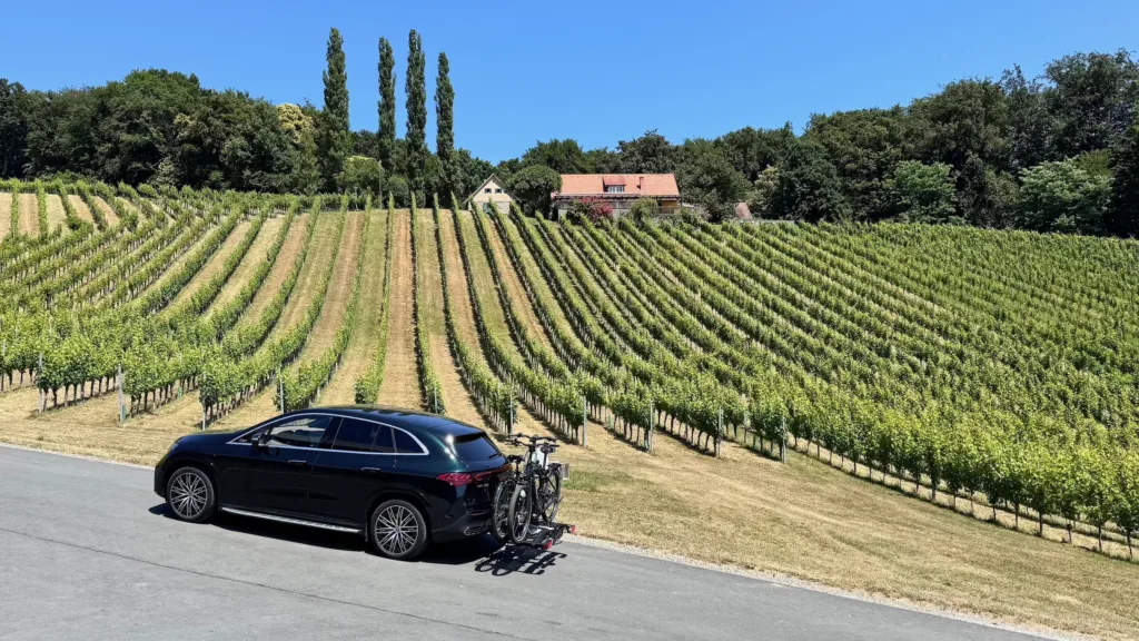 Samochód elektryczny Mercedes EQE SUV z bagażnikiem rowerowym na tle winnicy w Styrii