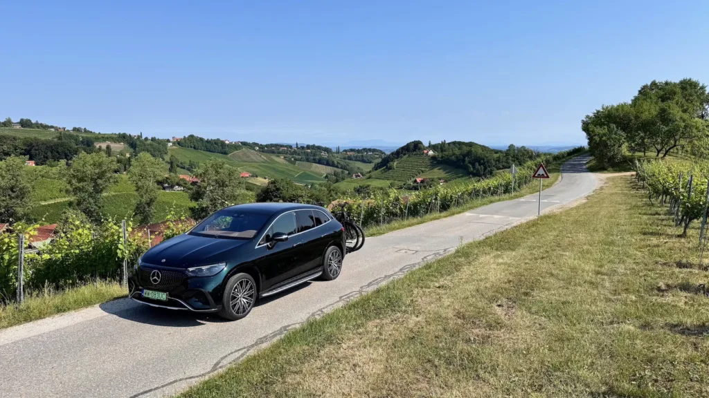 Samochód elektryczny Mercedes EQE SUV z bagażnikiem rowerowym na tle winorośli w Styrii (Austria)