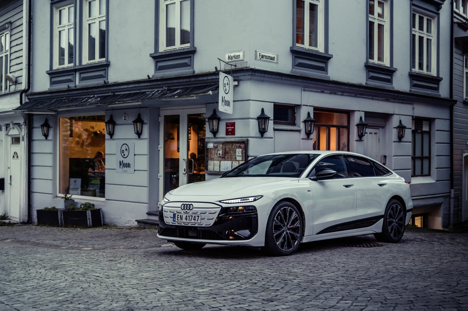 An Audi A6 Sportback e-tron in Glacier white metallic is parked in front of a restaurant in the Norwegian city of Bergen.
