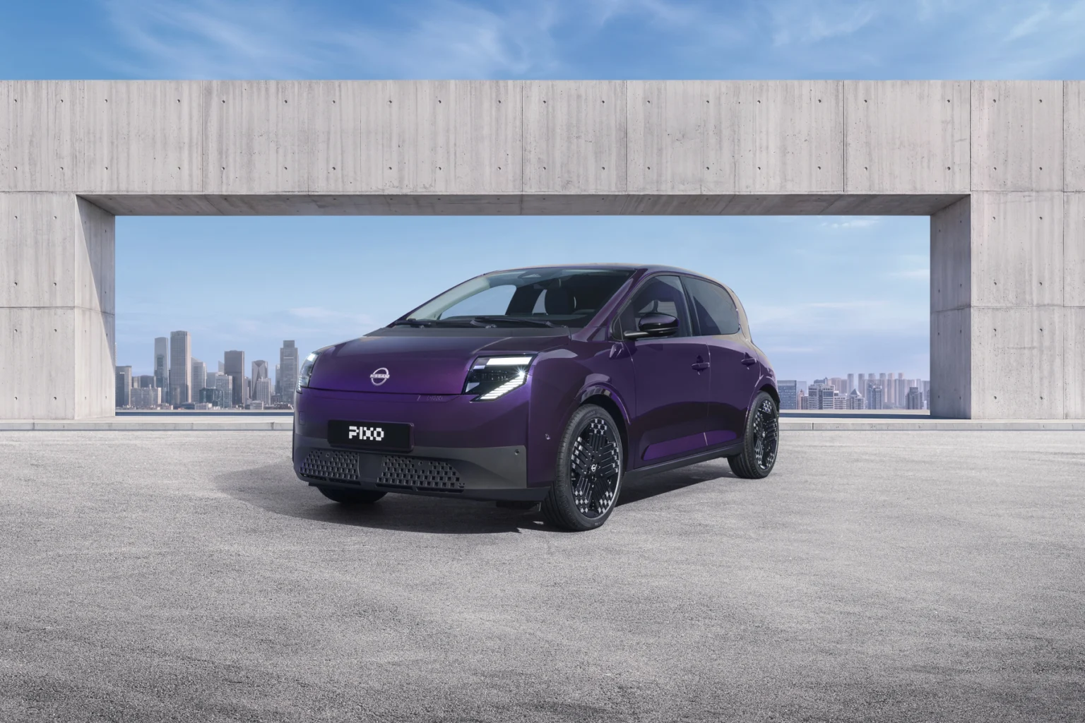 Three-quarter front view of a purple Nissan PIXO electric city car parked beneath a modern concrete structure, with a city skyline in the background.